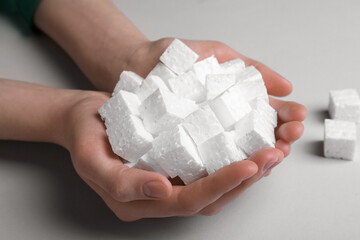 Woman with handful of styrofoam cubes on light grey background, closeup