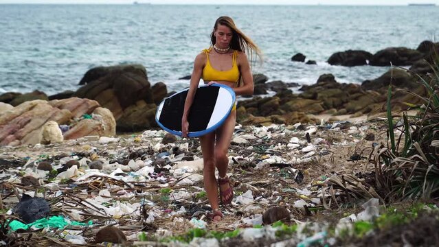 Caucasian young woman surfer walking on polluted beach wearing sandals over plastic bag waste garbage trash