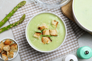 Bowl of delicious asparagus soup served on light grey table, flat lay