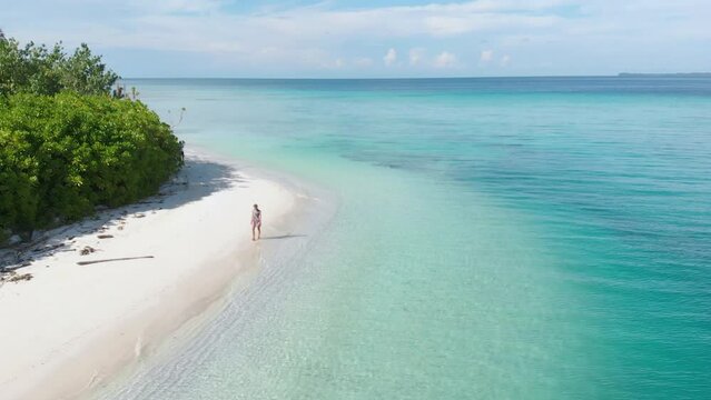 Aerial slow motion: adult woman walking on tropical beach turquoise water caribbean sea white sand green coconut palm trees Banyak Islands Indonesia travel destination sunny day