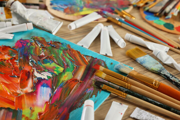 Obraz premium Set of different brushes, paints and abstract picture on wooden table, closeup