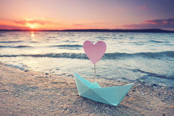 romantic sunset with colorful paper boat at the beach