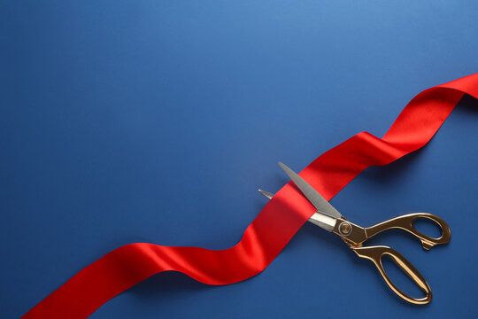 Red ribbon and scissors on blue background, top view. Space for text