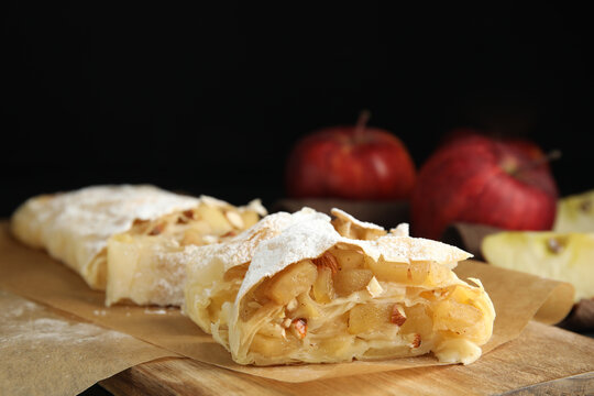 Delicious apple strudel with almonds and powdered sugar on wooden board, closeup. Space for text