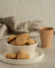 Сottage layer cookies with sugar and cinnamon in the white ceramic bowl on the white ceramic plate, ceramic glass with black coffee, linen kitchen towel