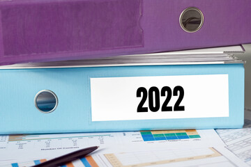 2022 on a blue file folder on a white surface on the bottom and violet folder on the top