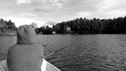 Black and white photo of a woman from behind, resting while fishing with a fishing rod on a sunny and cloudy afternoon.