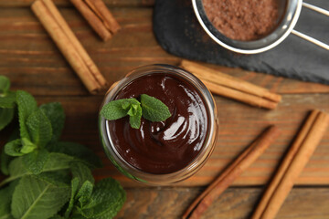 Glass of delicious hot chocolate with fresh mint and cinnamon sticks on wooden table, flat lay