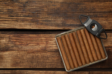Cigars and guillotine cutter on wooden table, top view. Space for text