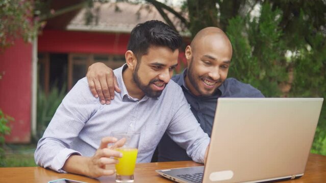 Gay black couple searching online together and looking at screen. Affectionate couple browsing on the internet and drinking orange juice.