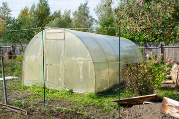 Greenhouse on a small farm. Summer day outside. Temporary fence for the land plot.