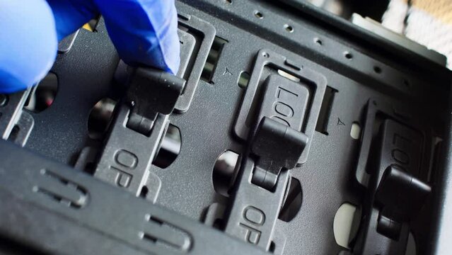 A blue gloved hand opens the switches from the Lock to the Open position. The master opens the electronic locks. Part of electronic equipment. Computer server room. Plastic and metal. Close-up