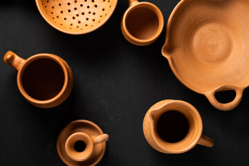 Clay pots for cooking. Light clay clay pots. Baking tins on a dark background. Earthenware: colander, plate, grocery, candlestick. Vintage kitchen utensils for cooking.