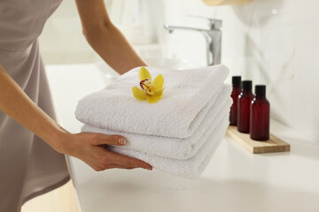 Chambermaid holding fresh towels with flower in hotel bathroom, closeup
