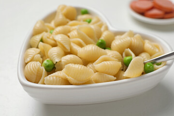 Heart shaped bowl with tasty pasta and peas on white table, closeup
