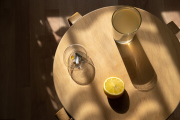 Top view of glass with bone broth, bowl with vitamins and lemon on small wooden table with deep shadows from sunlight. Sunny morning.