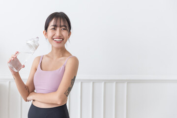 Fototapeta na wymiar Asian woman with long black hair tied up, happy smiling at the camera wearing sportswear and holding a water bottle standing on a white background. Active lifestyle image with copy space.