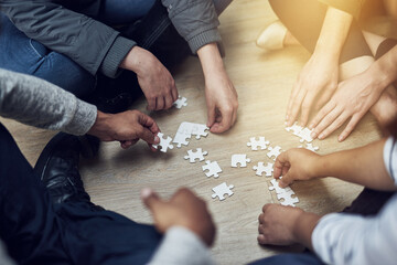 Start small and grow. Shot of a group of people building a puzzle together.