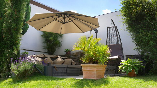 Gartenterrasse mit Loungegruppe und Sonnenschirm in einer Gartenecke mit Säulen-Faulbaum und umgeben von Pflanzen und Zypressen	