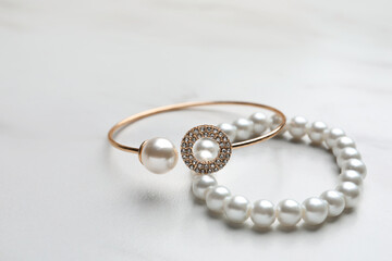 Elegant bracelets with pearls on white marble table, closeup