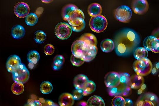 Soap bubbles are an extremely thin film of soapy water enclosing air that forms a hollow sphere with an iridescent surface. Gliding colorful bubbles isolated on black background with reflections.
