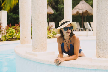 Joven modelo latina tomando el sol junto a la piscina de un resort todo incluido
 - obrazy, fototapety, plakaty