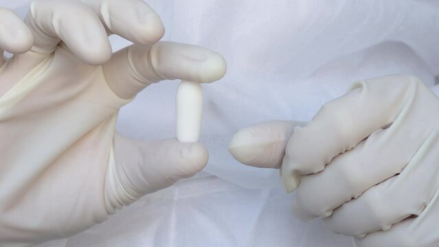 Suppositories in woman hands, white gloves. nurse or doctor, medical assistant, in white disposable robe holds a suppository in plastic pack. Suppository for anal or vaginal use. temperature, fever