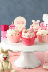 Obraz na płótnie Canvas Beautifully decorated baby shower cupcakes for girl with cream and toppers on pink wooden table