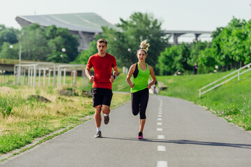 Obraz premium Full-length front view of an attractive caucasian couple running together in a park on a sunny day..