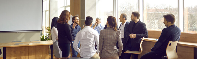 Business coach meeting with group of people in modern office interior. Team of workers listening to teacher's inspirational speech during creative business training class. Banner, header background - obrazy, fototapety, plakaty