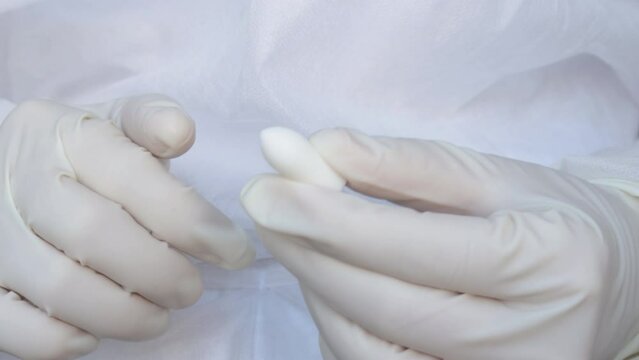 Suppositories in woman hands, white gloves. nurse or doctor, medical assistant, in white disposable robe holds a suppository in plastic pack. Suppository for anal or vaginal use. temperature, fever