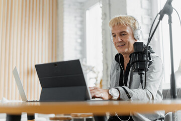 A man works as a presenter at a radio station , broadcasts using a microphone and a laptop