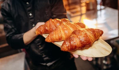 Foto op Plexiglas Handsome baker in uniform holding freshly baked croissants at the bakery © bondvit