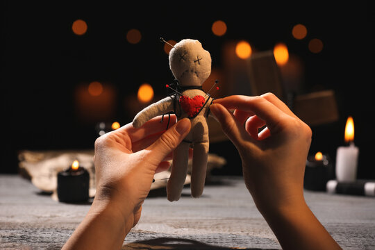 Woman stabbing voodoo doll with pin at wooden table indoors, closeup