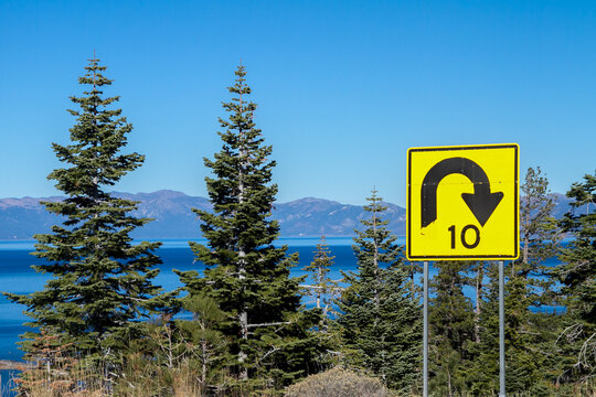 Mountain road overlooking an alpine lake with a severe traffic warning about a tight turn approaching. 