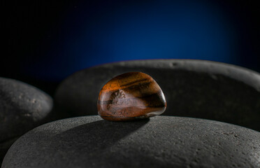 Eye of a tiger stone, on a rock in the darkness  with a rim light and a dark blue background