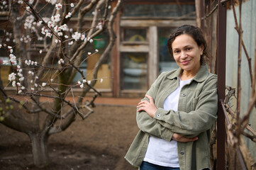 Confident middle aged Caucasian woman gardener enjoying an early spring day standing in her garden...