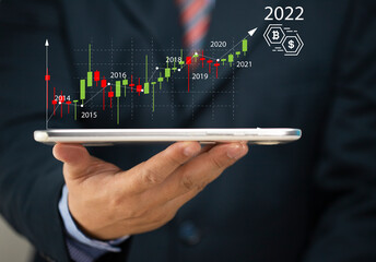 Businessman holding tablet 2022 stock market forecast outlook in his hand, charts and candlesticks, stock market movement trend, past to present.