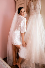 Sexy bride in the boudoir posing with a wedding dress. Happy young girl in a pink room.