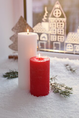 Beautiful burning candles with Christmas decor near window