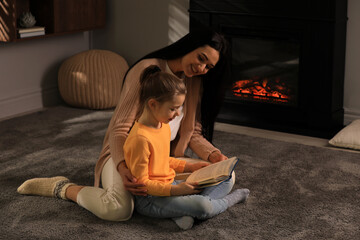 Happy mother and daughter reading together on floor near fireplace at home