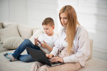 A busy mom works at a computer. Son shows funny videos to mom. Mom works and sits with the baby at home.