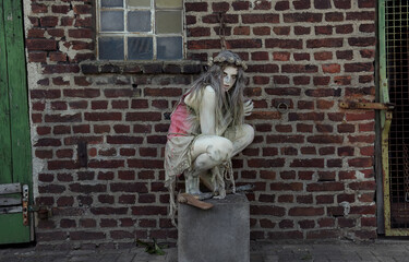 A teenage girl is dressed in rags as a Halloween horror 
figure. She sits on a cement block with a...