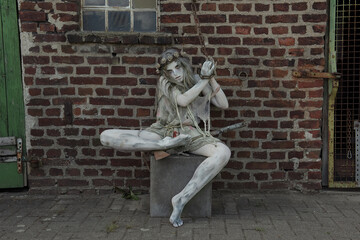 A teenage girl is dressed in rags as a Halloween horror 
figure. She sits on a cement block with a...