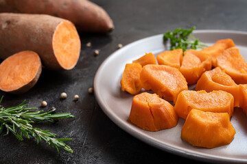 Roasted sweet potatoes and raw yam on a dark table close-up, plant based dining concept