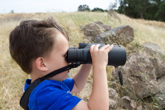boy on adventure exploring hillside bird watching and lost using binoculars to find his way home without a guide showing the right direction.  Adventurous courageous boy determined to find his way.
