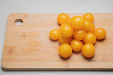 A heap of yellow cherry tomatoes on a wooden cutting board in the kitchen on a white table