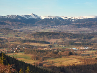 The spring landscape of Rudawy Janowickie at sunrise with the snow-covered Karkonosze Mountains in the background. Horizontal view from the top Sokolik Big on forests, fields and mountains. - obrazy, fototapety, plakaty