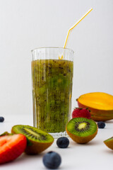 Kiwi juice in glass with a straw, fruits scattered on the table, healthy tasty sweet drink