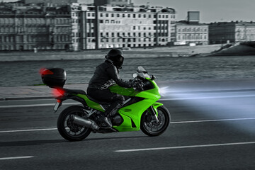 Fototapeta na wymiar A woman rides a motorcycle in the night city. Motorcyclist rides along the embankment on a green sports bike. Motorcycle travel. Headlights at night.